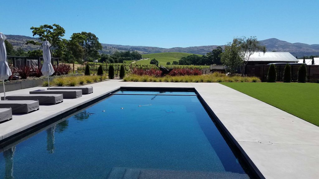 swimming pool with graded concrete and lawn on either side, overlooking vineyard countryside