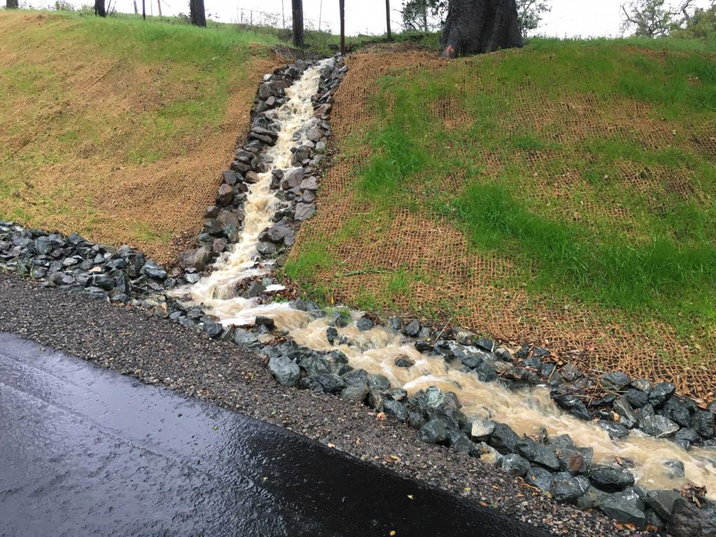 water rushing down a gulley of a small hillside toward a graded drain